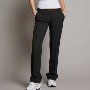Svarta kostymbyxor - Snygga svarta kostymbyxor med en klassisk straight passform. Byxorna har en midwaist design och är perfekta för en stilren look. De har diskreta fickor och en dragkedja framtill.