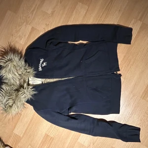 Mörkblå hoodie från Abercrombie & Fitch - Säljer en snygg mörkblå hoodie från Abercrombie & Fitch med fuskpälsfodrad huva. Jackan har dragkedja och två fickor framtill. Perfekt för kyliga dagar!