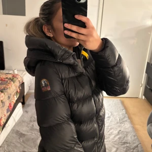 Svart dunjacka från Parajumpers - Säljer en svart lång dunjacka från Parajumpers med huva och dragkedja. Jackan har en quiltad design och en logotyp på ärmen. Perfekt för kalla dagar. Skit snygg direkt från johnells. 