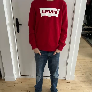 Snygg rött tröja från Levis - Säljer en snygg klassisk Levi’s-tröja i storlek 164 cm (14A). Tröjan har en ikonisk vit Levi’s-logga på bröstet och är tillverkad i mjuk bomull med ribbade muddar för en bekväm passform. Perfekt för en avslappnad stil eller vardagsbruk.  Personen på bilderna är 160 cm lång, 12 år gammal och har en smal/normal kroppsbyggnad.  Skick: Bra begagnat skick utan synliga skador eller fläckar.  Nypris: 400 SEK