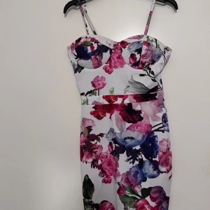 Blommig klänning från Parisian - Snygg blommig klänning från Parisian med smala axelband och dragkedja i ryggen. Klänningen har en färgglad design med rosa, lila och gröna blommor på en vit bakgrund. Perfekt för sommarens festligheter!