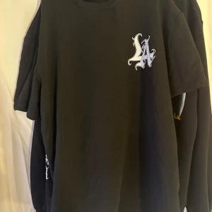 Svart t-shirt med tryck från SMOG - Cool svart t-shirt från SMOG med stort LA-tryck och texten 'Trust No One Only Yourself' på baksidan. Perfekt för en avslappnad stil med en edgy touch. 