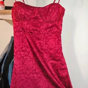 Vinröd klänning med blommigt mönster - Snygg vinröd klänning med blommigt mönster och smala axelband. Perfekt för en elegant kväll med sin figurnära passform och vackra detaljer.