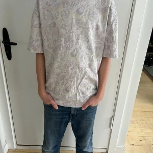 Vit t-shirt med mönster från H&M - Säljer en vit H&M T-shirt i storlek XS (passar ca 175 cm). T-shirten har ett ljust MTV-inspirerat tryck och är i relaxed fit. Tillverkad av mjuk bomull, perfekt för en avslappnad vardagsstil.  Personen på bilderna är 160 cm lång, 12 år gammal, och har en smal/normal kroppsbyggnad.  Skick: Bra begagnat skick, med minimala tecken på användning.  Nypris: 150 SEK