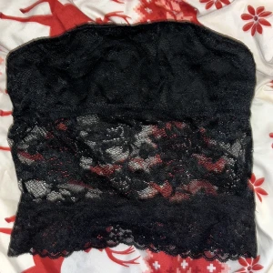 Fest Svart spets tubtopp - Snygg svart tubtopp i spets med ett elegant mönster. Perfekt för en kväll ute eller en speciell tillställning. Toppen är axelbandslös och har en fin spetsdetalj som ger en romantisk känsla.