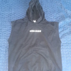 Svart ärmlös hoodie från Lindex - Säljer en svart ärmlös hoodie från Lindex med texten 'WALLRIDE' på bröstet. Perfekt för en avslappnad stil. Tillverkad i Turkiet.