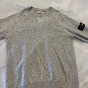Grå tröja från Stone Island - Säljer en stilren grå tröja från Stone Island i storlek M. Tröjan har en rund halsringning och ribbade muddar vid ärmslut och nederkant. Perfekt för en avslappnad look. Den är använd några gånger och säljs då den intr passar min stil längre. Priset är inte hugget i sten vid snabb affär!