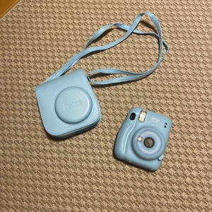 Blå Instax Mini 11 kamera med väska - Säljer en ljusblå Instax Mini 11 kamera med matchande väska. Kameran har en kompakt design och är perfekt för att ta omedelbara bilder. Väskan har en axelrem för enkel transport. Den är i nyskick och ändats använd fåtal gånger. Skriv om du har några frågor och för prisförslag! ☺️