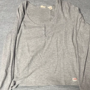 Grå ribbad tröja från Levi's - Säljer en stilren grå ribbad tröja från Levi's med rund hals och tre knappar framtill. Perfekt för en avslappnad look.