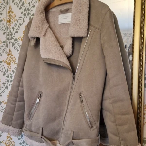 Beige jacka med fuskpäls från Zara - OT Zara schearling jacket i fuskmocka. Varm och skön med lurvigt foder. Känns tung och lyxig. Har tyvärr inte kommit till användning så säljer nu vidare.  Storlek M, rymlig, passar även för en liten L Inga anmärkningar