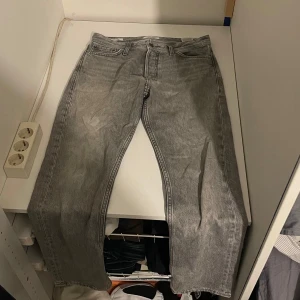 Grå jeansbyxor från Jack and Jones  - Snygga grå jeansbyxor med klassisk femficksdesign och dragkedja. Perfekta för en avslappnad stil. Jack and Jones 