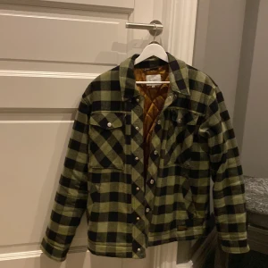 Rutig jacka från Vailent/charlings - Snygg rutig jacka från Vailent i svart och grön med quiltat foder. Jackan har knappar framtill och två bröstfickor med lock. Perfekt för höst och vår.