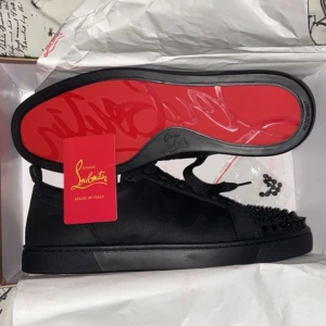 Svarta Christian Louboutin - Snygga svarta sneakers i skinn från Christian Louboutin med ikonisk röd sula. Skorna har svarta nitar på tån och snörning för en edgy look. Perfekta för att ge din outfit en unik touch.