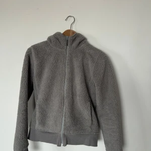 Grå fleecejacka från Uniqlo - Mysig grå fleecejacka från Uniqlo med dragkedja och huva. Perfekt för kyliga dagar med sin mjuka och varma känsla. Jackan har långa ärmar och en enkel design som passar till det mesta.