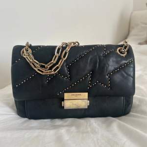 Black lamb skin Ziggy bag from Zadig & Voltaire featuring a quilted effect, micro stud details, a rectangular body, a foldover top with clasp closure, gold-tone hardware and a chain shoulder strap. This bag can be worn crossbody and as one shoulder. 