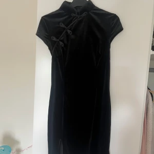Svart klänning - Sammets-liknande material. Åtsittande med slits nedtill på ena sidan. Knappar går att knäppa upp. Liten i storleken. Aldrig använd