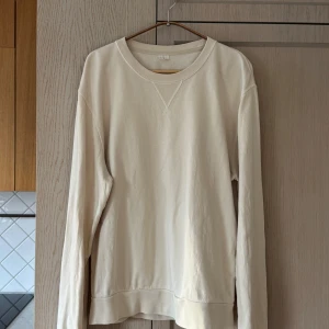Ljusbeige långärmad tröja från Arket - Storlek L - Säljer en stilren ljusbeige långärmad tröja från Arket i  bra använt skick. Perfekt för både vår och höst. Tröjan är gjord i mjuk bomull och har en klassisk rund halsringning. Passar till alla tillfällen, från chill hemma till en dag på stan. Små defekter i form av några små hål som visas på sista bilderna och som inte påverkar komforten.