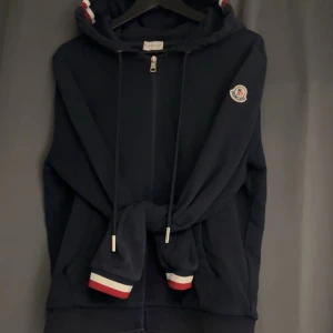 Mörkblå Moncler Hoodie. - Säljer en snygg mörkblå hoodie från Moncler. Bra skick köpte den för ungefär 1 år sen av en kille här på plick. Har tagit hand om den. Den har ett litet hål på magfickan som inte syns om man t.ex har en svart t-shirt under tröjan. Inget kvitto finns.  