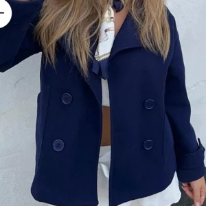 Mörkblå kappa Design by si  - Säljer en stilren mörkblå kappa i mycket bra skick. Den har en klassisk dubbelknäppning med stora knappar och långa ärmar. Perfekt för höst och vår, och funkar både till vardags och lite finare tillfällen. Passar bra över en tröja eller blus. 🧥💙