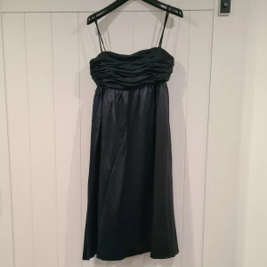 Svart festklänning - Snygg svart klänning med smala axelband och rynkad detalj vid bysten. Klänningen har en elegant och enkel design.