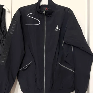 Svart vindjacka från Jordan - Säljer en svart vindjacka från Jordan i storlek S. Den har en dragkedja framtill och två fickor med dragkedjor. Perfekt för sportiga aktiviteter eller som en stilren vardagsjacka. Jackan har en liten logga på bröstet och är i grymt skick!