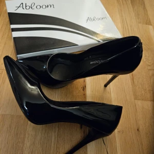 Svarta pumps från Abloom - Snygga svarta pumps helt nya från Abloom. De har en elegant spetsig tå och hög klack, perfekta för festliga tillfällen. Skorna är gjorda i ett glänsande syntetmaterial som ger en lyxig känsla. Kommer i originalkartong.