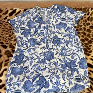 Blommig blus från H&M - Säljer en superfin blommig blus från H&M i storlek 42. Den har ett vackert blått blommönster på vit bakgrund och korta ärmar. Perfekt för vår och sommar! 🌸