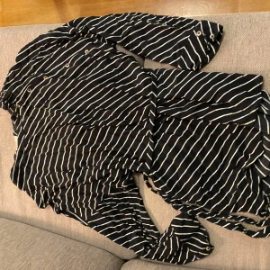 Svart och vit randig klänning från Dobber - Snygg marinblå och vitrandig klänning från Dobber i storlek L. Klänningen har långa ärmar och knappar framtill, vilket ger en stilren look. Perfekt för både vardag och festliga tillfällen. Materialet känns mjukt och bekvämt.