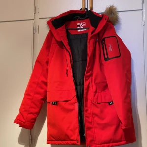 Röd vinterjacka från True North - Säljer en snygg röd vinterjacka från True North i storlek medium. Jackan har en mysig pälskant på huvan och flera praktiska fickor med dragkedja. Perfekt för kalla nordiska vintrar! 🧥❄️