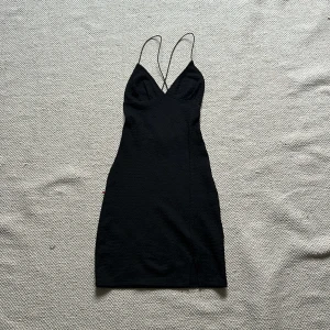 Svart klänning från H&M Divided - Snygg svart klänning från H&M Divided i storlek XXS. Den har tunna axelband och en djup v-ringning, perfekt för festliga tillfällen. Materialet är mjukt och stretchigt, vilket ger en bekväm passform. Klänningen är kort. Öppen rygg. Skriv för fler bilder eller frågor 