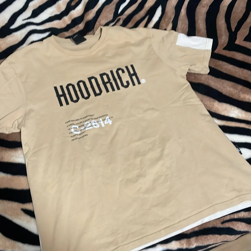 En Hoodrich T-shirt i beige färg i storlek XL men passar även L då den är liten i storlek. Skick 8/10 använd fåtal gånger . T-shirts.