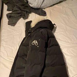 Svart dunjacka med pälsdetalj - Säljer en svart äkta Moose knuckles vinterjacka i storlek L/G med äkta päls också. Jackan har en dragkedja framtill och praktiska fickor med dragkedjor. Perfekt för kalla vinterdagar! Tyvärr finns inget kvitto