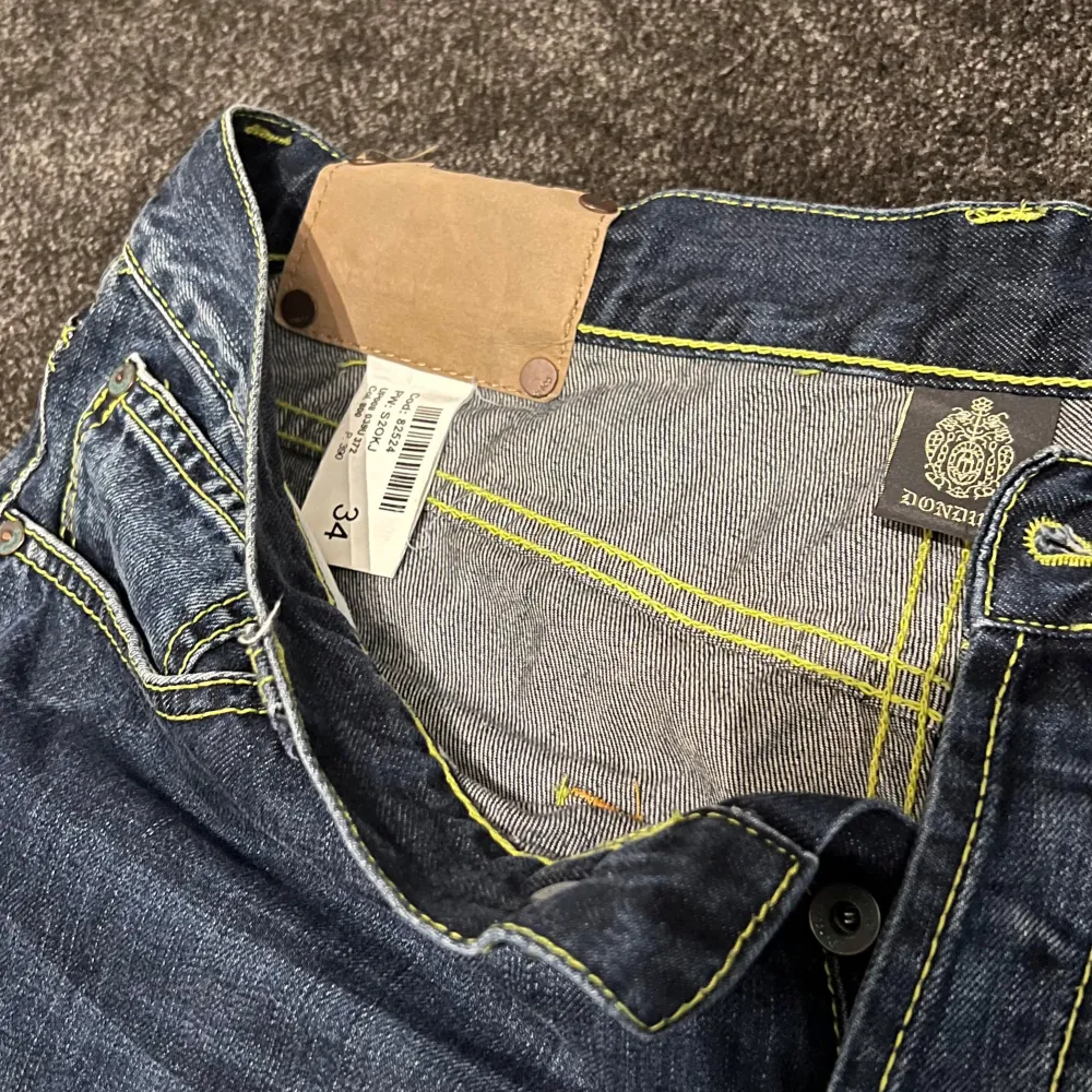 Säljer ett par snygga blå jeans från Dondup. De har en klassisk femficksdesign med gul kontrastsöm som ger en cool look. Jeansen är i bra skick och har en knappgylf. Perfekta för vardagsbruk eller en avslappnad utekväll!. Jeans & Byxor.