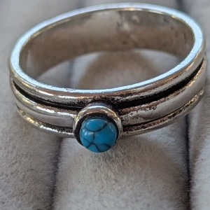 Silverring med turkos sten - Säljer en snygg silverring med en liten turkos sten i mitten. Ringen har en enkel men stilren design med dubbla linjer som ramar in stenen.koppar material storlek 11 ( 20.7 diameteren)