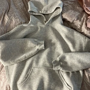 Grå hoodie - Säljer en klassisk grå hoodie med känguruficka och justerbar huva. Perfekt för en avslappnad stil. Passar bra till jeans eller mjukisbyxor.