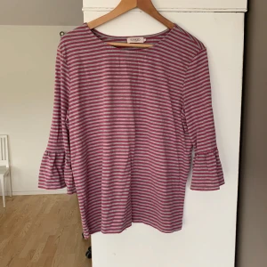 Randig topp från Soaked in Luxury - Säljer en randig topp från Soaked in Luxury i rosa och grått. Toppen har trekvartsärmar med volangdetaljer. Priset går att diskutera vid en snabb affär. Tveka inte med att höra av dig om du har funderingar eller frågor.