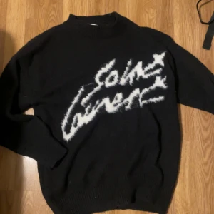 Saint Laurent tröja  - Eftertraktad Snygg svart tröja från Saint Laurent med ett iögonfallande vitt mönster på framsidan. Tröjan har långa ärmar och en klassisk passform. Perfekt för en stilren look. Helt ny, använder inte då den är för liten för mig. Tar gärna byten 