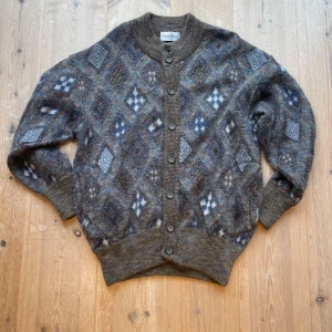 Mönstrad kofta från Gianni Bugli - Säljer en unik mönstrad kofta från Gianni Bugli mörkare färger. Koftan har ett geometriskt mönster med knappar framtill och ribbade muddar vid ärmslut och nederkant. En riktigt härlig cardigan för dig som vågar dig på något nytt! Storleken är ungefär en liten M