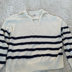 Vit och marinblå randig tröja från Nelly - Säljer en stilren vit tröja med marinblå ränder från Nelly. Tröjan har en v-ringad krage och långa ärmar, perfekt för en avslappnad look. Den är gjord i ett mjukt material. Tröjan är endas använd ett fåtal gånger och inga synliga defekter!