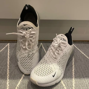 Vita Nike Air Max 270 sneakers - Snygga vita Nike Air Max 270 sneakers med svart detalj och synlig luftenhet i hälen. Skorna har snörning och en modern design som passar perfekt för en sportig look. Skorna är sparsamt använda och det finns inga hål eller separationer. OBS! Saknar innersulor.