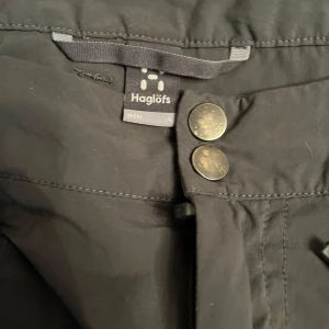 Svarta byxor från Haglöfs - Snygga svarta byxor från Haglöfs med dragkedjor på fickorna och knappar i midjan. Perfekta för utomhusaktiviteter med sin funktionella design och slitstarka material.
