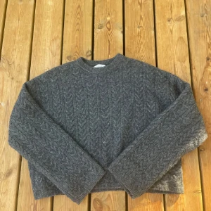 Grå stickad tröja från Zara - Säljer en mysig grå stickad tröja från Zara med kabelstickat mönster. Tröjan har långa ärmar och en rund halsringning, perfekt för kyliga dagar.