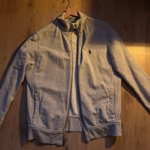 Grå tröja från Polo Ralph Lauren - Säljer en stilren grå tröja från Polo Ralph Lauren med dragkedja och broderad logga på bröstet. Perfekt för en avslappnad look. Tröjan har långa ärmar och en bekväm passform. 500kr, pris går att diskutera (nypris 2100)