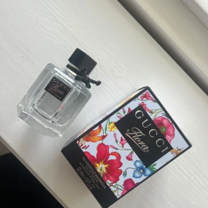 Gucci Flora Glamorous Magnolia Parfym - Gucci Flora Glamorous Magnolia parfym i en elegant, fyrkantig glasflaska med svart kork och en liten svart rosett. Förpackningen är dekorerad med färgglada blommor som ger en lyxig känsla. Perfekt för den som älskar blommiga dofter. Helt oanvänd, köpt på flygplats