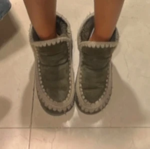 Mou skor  - Säljer ett par gröna Mou vinter skor med stickade detaljer runt kanterna. De har en mysig och varm design, perfekt för kyligare dagar. Bootsens unika stil gör dem till ett trendigt val för höst och vinter.