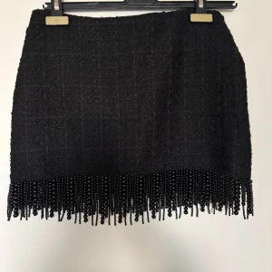 Svart kjol med pärlor MANGO - Snygg svart kjol med pärldetaljer längs nederkanten. Perfekt för att ge en elegant touch till din outfit. Kjolen har en klassisk passform och är lätt att matcha med olika toppar.