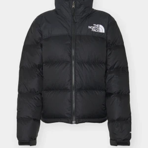 Svart dunjacka från The North Face - Säljer en svart dunjacka från The North Face med dragkedja och hög krage. Jackan har en pufferdesign och är perfekt för kyliga dagar. Den har långa ärmar och logotypen syns både fram och bak. En stilren och funktionell jacka för vintern. Använt fåtals ggr, inga defekter. Nypris 2795, säljs för 1500kr!