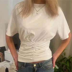 Vit kortärmad topp med rynkdetalj - Snygg vit topp med korta ärmar och rynkdetalj i midjan som ger en smickrande passform. Perfekt för en stilren och enkel look. Storlek L men passar mig som brukar ha S. Lånad bild💕