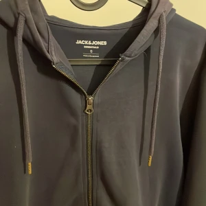 Mörkblå huvtröja från Jack & Jones - Säljer en stilren navy huvtröja från Jack & Jones Essentials. Tröjan har dragkedja framtill och justerbar huva med snören. Perfekt för en avslappnad look. Köpt för cirka 500 från hemsidan.