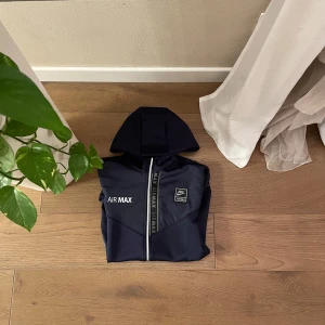 Svart hoodie från Nike Air Max - Nike Air Max sweatshirt in blue, size M, available in excellent condition. Made of soft and breathable material. The modern design and Nike Air Max logo make it a trendy piece, ideal for those who love a sporty and casual style. Easy to match with jeans or track pants, it is a must-have for every wardrobe. Don't miss the opportunity to add this versatile piece to your collection!